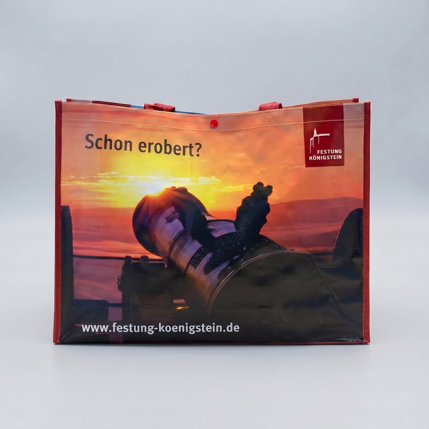 Mehrwegtasche, rote Umsäumung und Henkel, Bild mit aufgehender Sonne über Kanone, schwarze Schrift oben: Schon erobert? mit Logo, weiße Schrift unten: Internetadresse