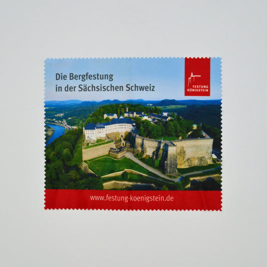 Luftbild Festung Königstein im Elbsandsteingebirge, wolkenloser Himmel darin schwarze Schrift: Die Bergfestung in der sächsischen Schweiz, daneben rotes Logo, ganz unten rot unterlegt die Internetadresse