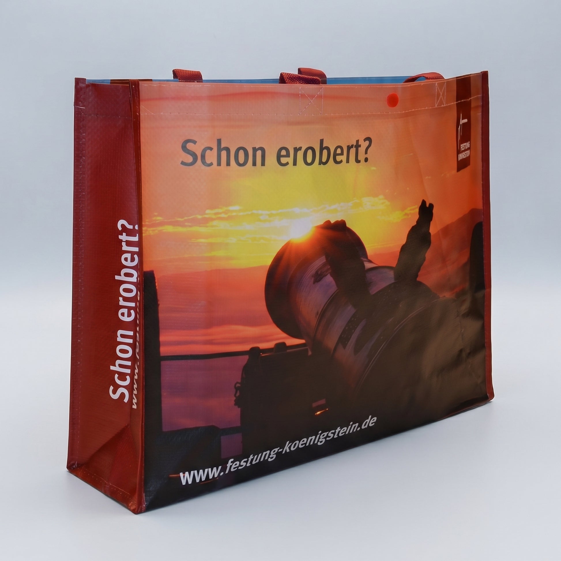 Mehrwegtasche, rote Umsäumung und Henkel, Bild mit aufgehender Sonne vorn, weiße Schrift auf roter Seite: Schon erobert? mit Internetadresse
