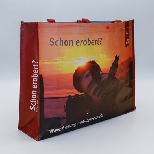 Mehrwegtasche, rote Umsäumung und Henkel, Bild mit aufgehender Sonne vorn, weiße Schrift auf roter Seite: Schon erobert? mit Internetadresse