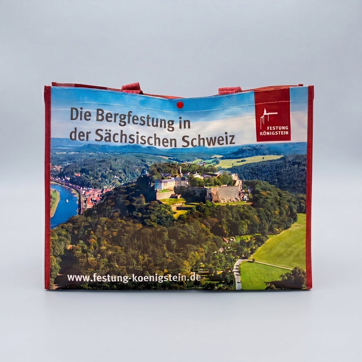 Mehrwegtasche, rote Umsäumung und Henkel,  Luftaufnahme der Festung Königstein mit Elbsandsteingebirge, blauer Himmel schwarze Schrift oben: Die Bergfestung in der sächsischen Schweiz mit Logo, weiße Schrift unten: Internetadresse