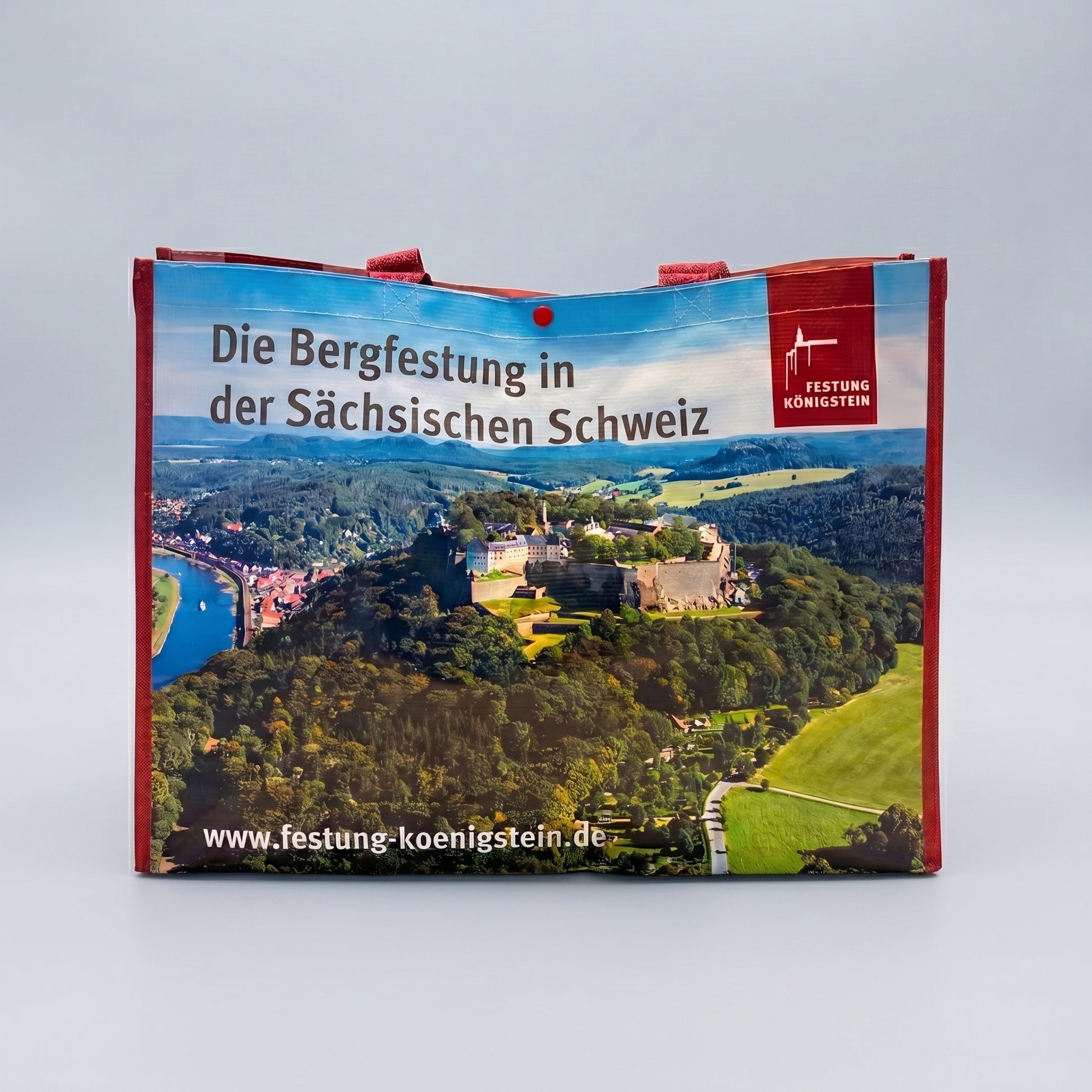 Mehrwegtasche, rote Umsäumung und Henkel,  Luftaufnahme der Festung Königstein mit Elbsandsteingebirge, blauer Himmel schwarze Schrift oben: Die Bergfestung in der sächsischen Schweiz mit Logo, weiße Schrift unten: Internetadresse