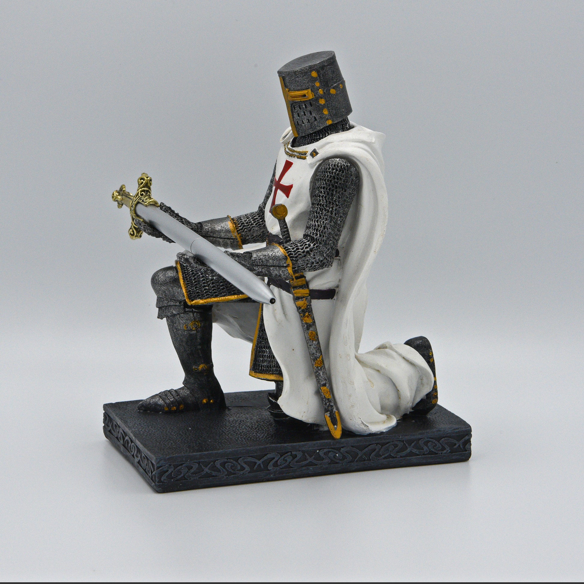 Ritter, anthrazit-silberner Rüstung, darüber weißes Templer-Hemd mit Umhang, Schwert an Hüfte, kniet auf Sockel und präsentiert ein  Schwert (Kugelschreiber) in silber mit goldenem Griff, Sicht von rechts