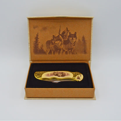 geöffnete helle Geschenkbox mit Wölfen im Deckel, darin Klappmesser, heller Griff mit Wölfen und Verzierungen