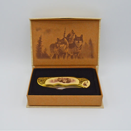 geöffnete helle Geschenkbox mit Wölfen im Deckel, darin Klappmesser, heller Griff mit Wölfen und Verzierungen