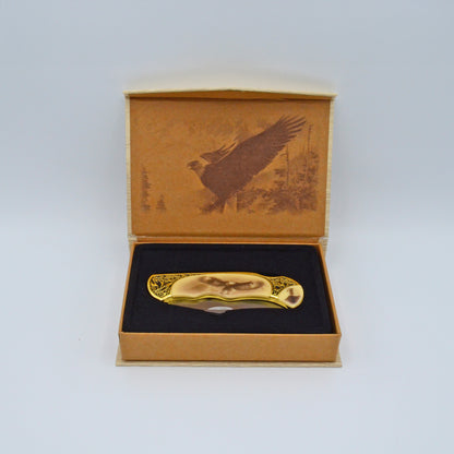 geöffnete helle Geschenkbox mit Adler im Deckel, darin Klappmesser, heller Griff mit Adler und Verzierungen
