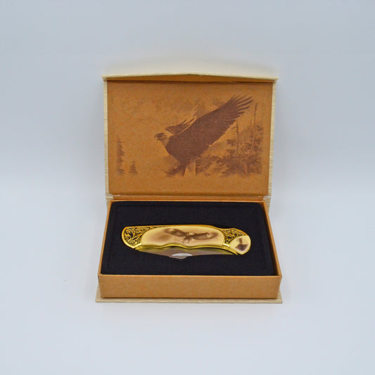 geöffnete helle Geschenkbox mit Adler im Deckel, darin Klappmesser, heller Griff mit Adler und Verzierungen