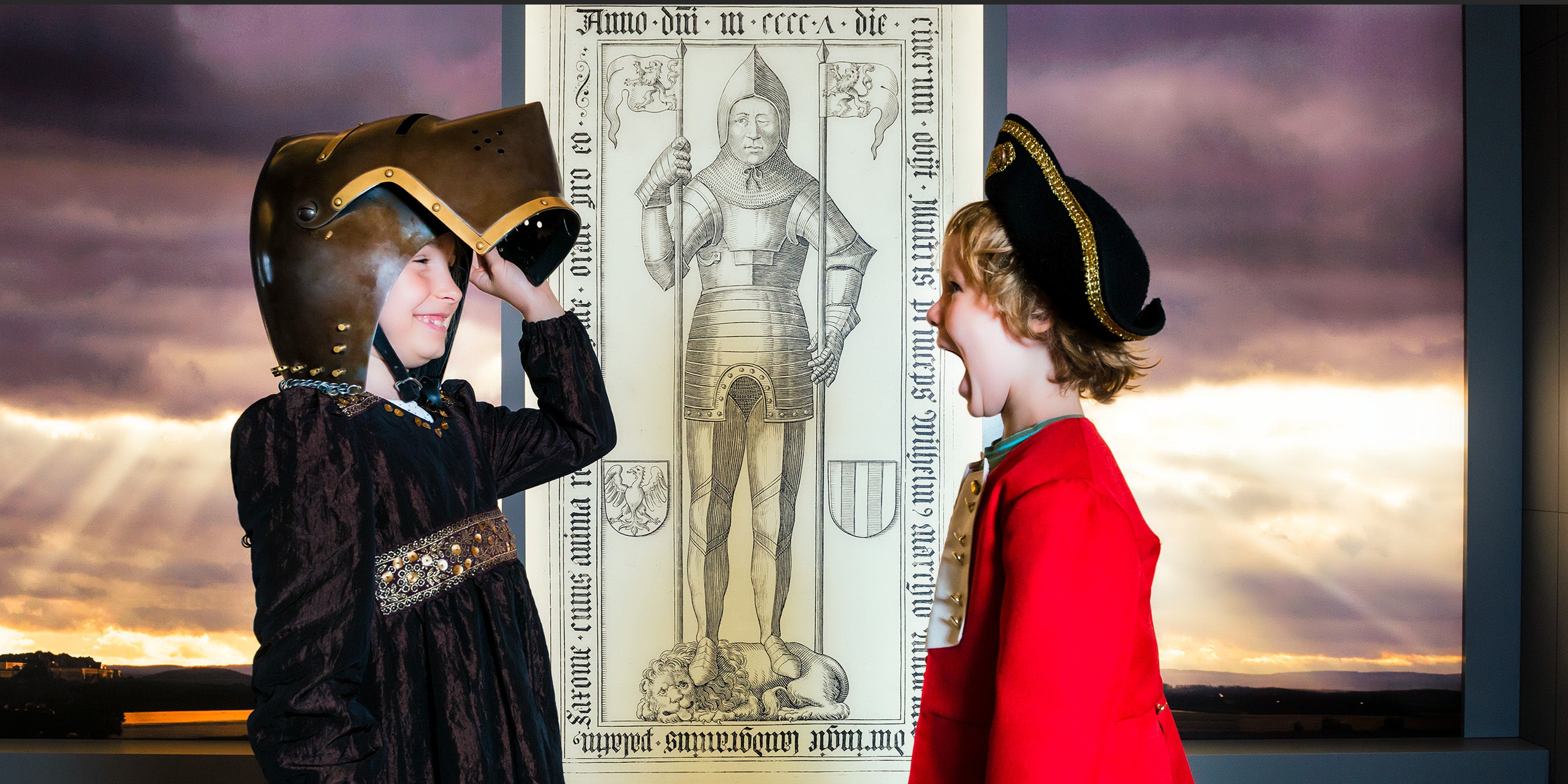 Mädchen im historischen Kleid setzt Ritterhelm auf, Junge im Clemens-Kostüm findet das gut