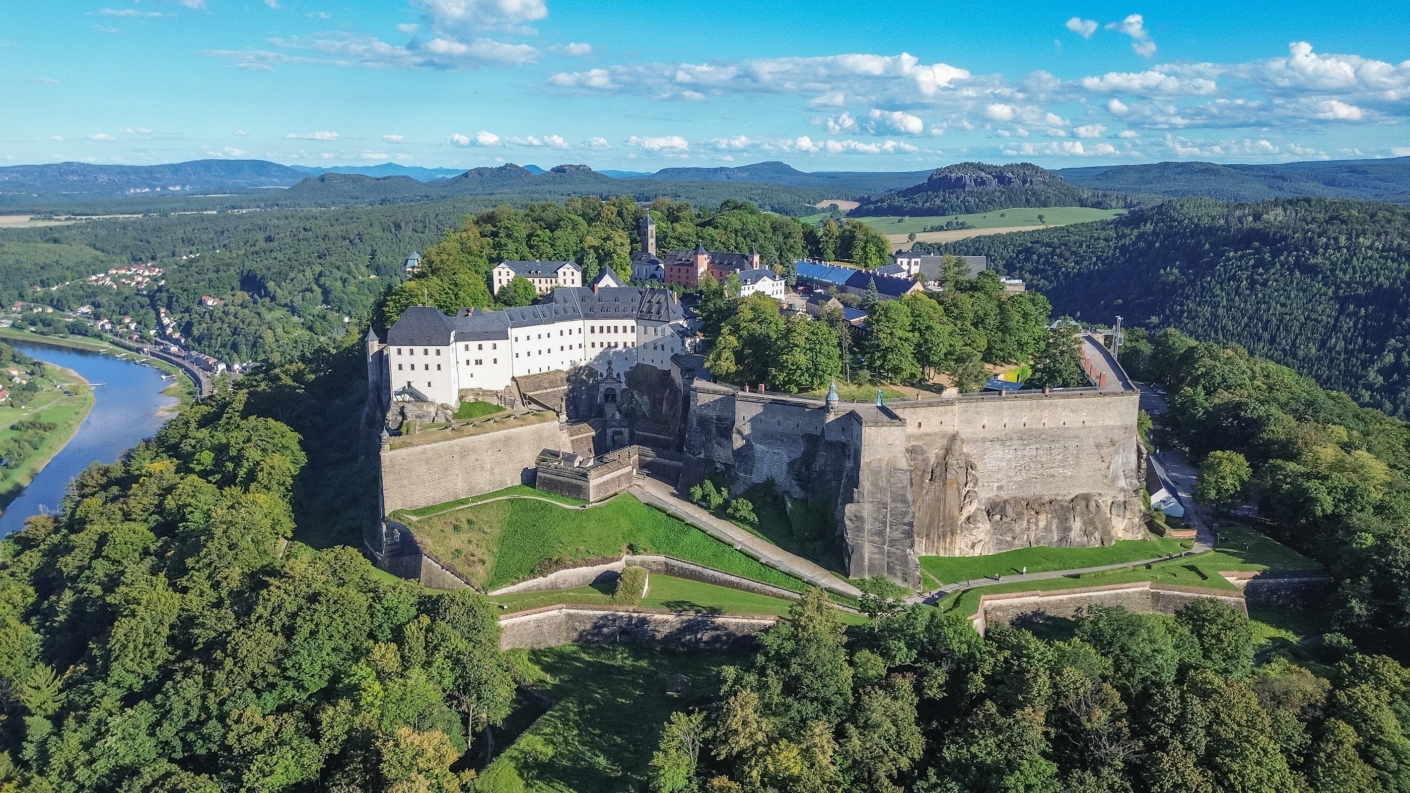 Luftaufnahme der Festung Königstein von Westen, mit Elbsandsteingebirge im Hintergrund, blauer Himmel mit wenig Wolken